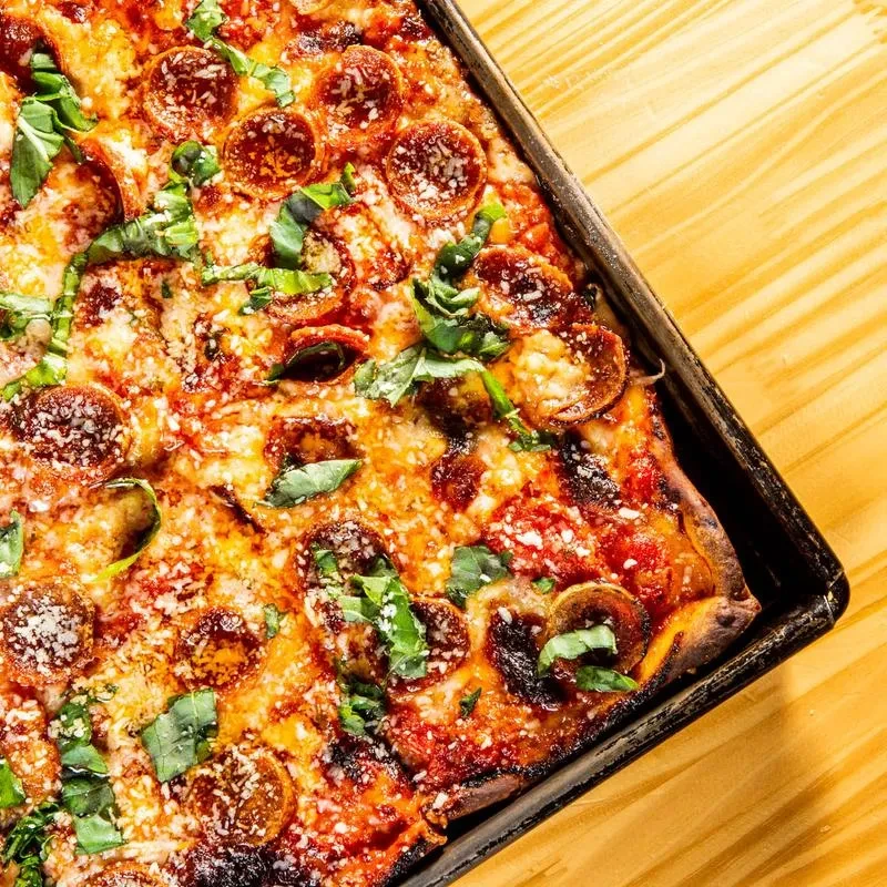 Rectangular pepperoni pizza with basil and Parmesan in a baking tray.