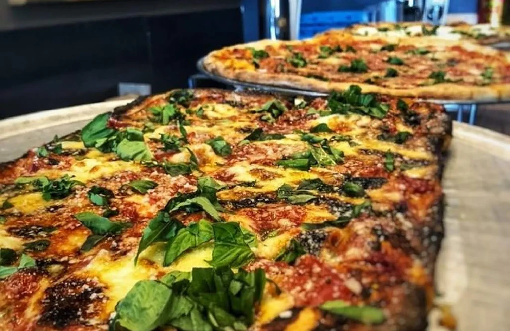 Charred square-cut pizza with mozzarella, tomato sauce, and fresh basil.