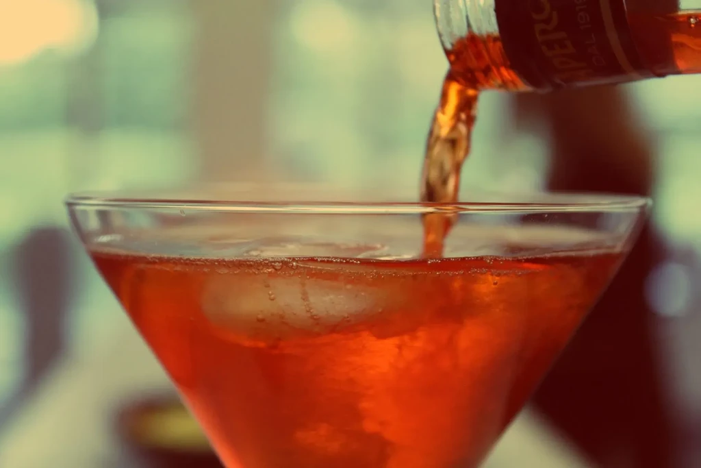 Orange-red Aperol poured into a martini glass with ice.