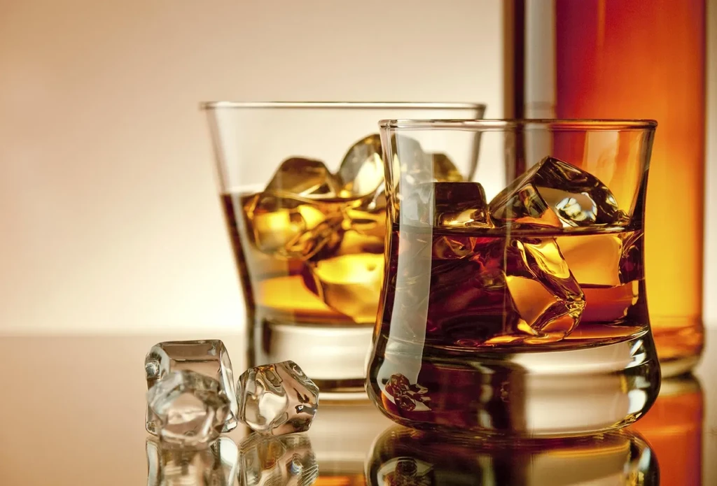 Two glasses of whiskey on ice with a partial bottle.