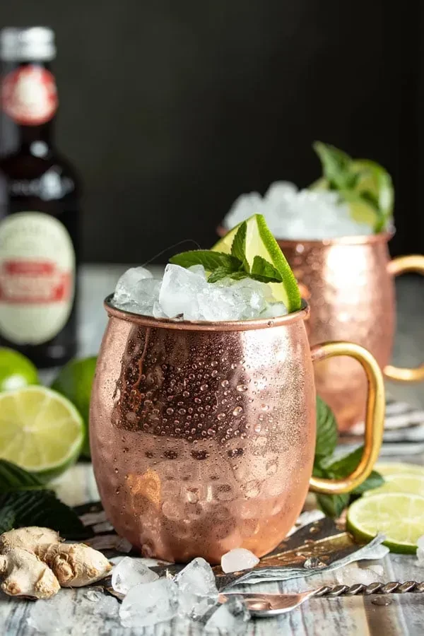 Two chilled copper mugs with Moscow Mules, limes, mint, ginger.