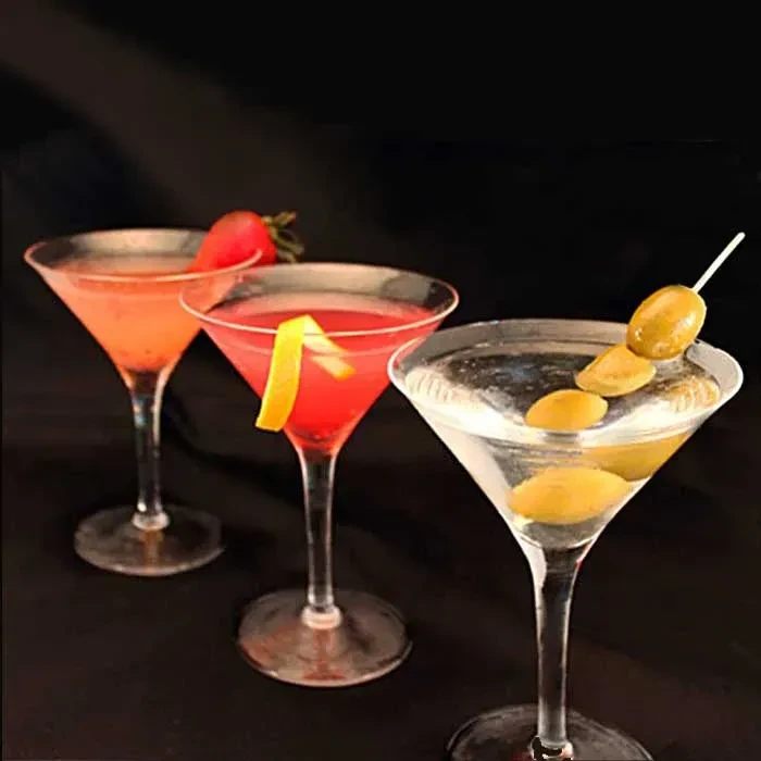 Three colorful cocktails in martini glasses garnished with strawberry, lemon, olives.
