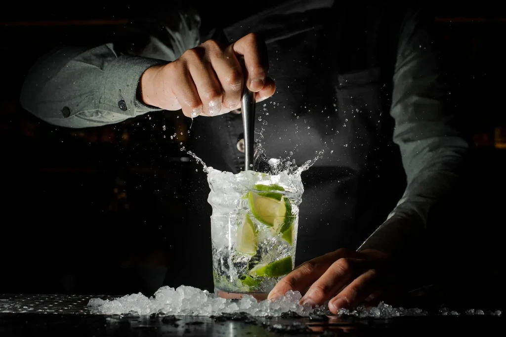 Bartender's hands stir drink with ice, lime, liquid splashing.