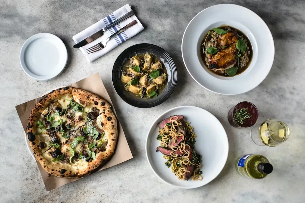 Overhead view: a diverse spread of pizza, pasta, steak, and drinks.