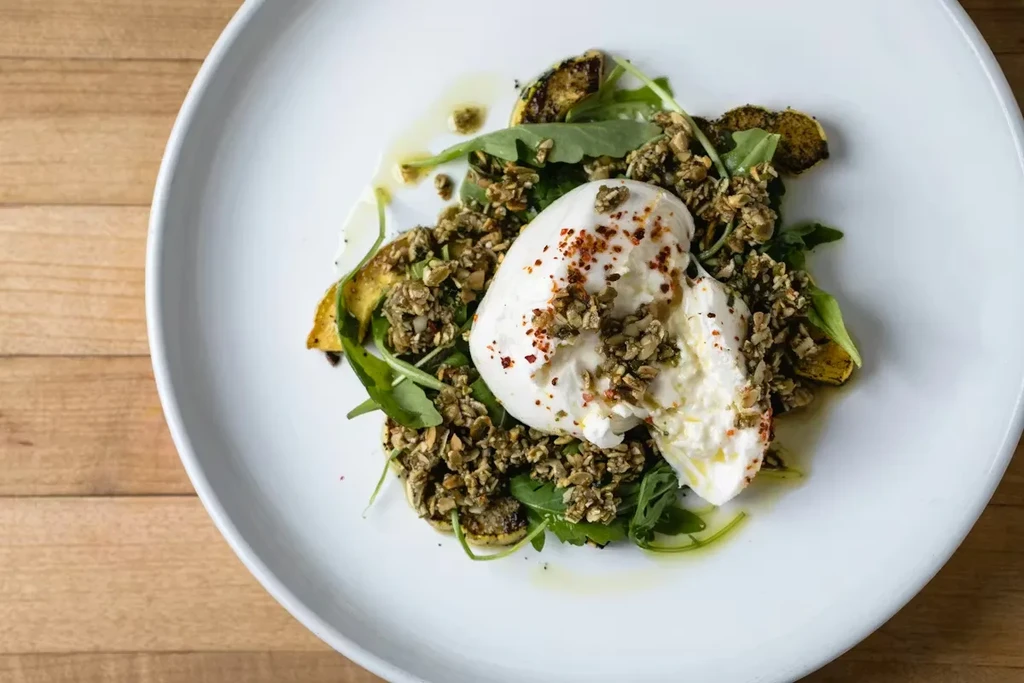 Plated burrata with chili flakes, arugula, squash, and savory granola.