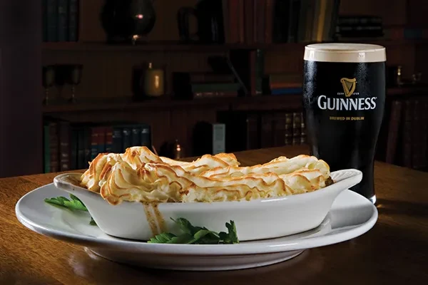 Golden gratin dish and a pint of Guinness on a wooden table.