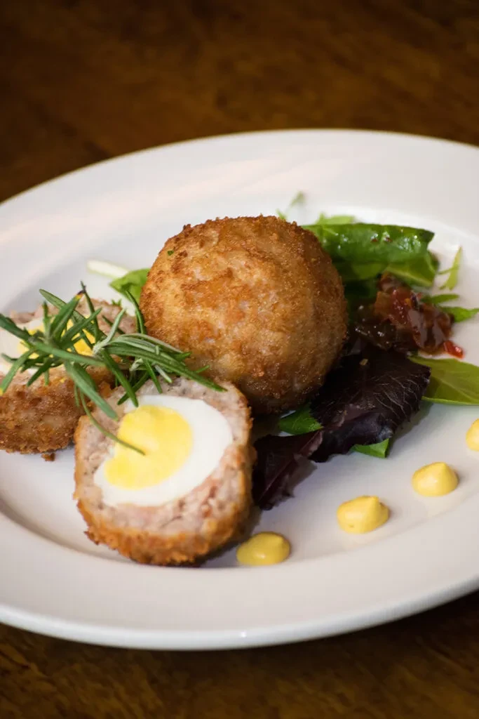 Two Scotch eggs, one halved, with salad, relish, and yellow sauce.