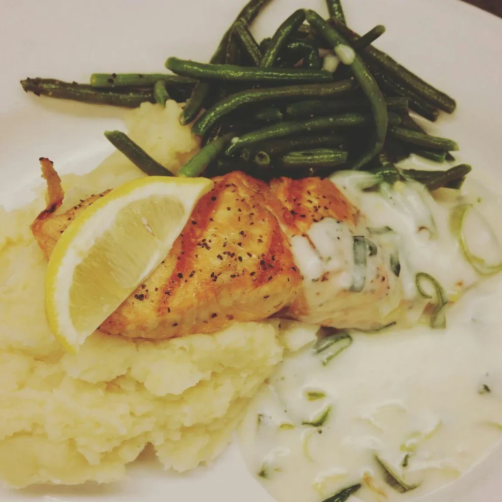 Overhead view: Plated fish, lemon, mashed potatoes, green beans, herb sauce.