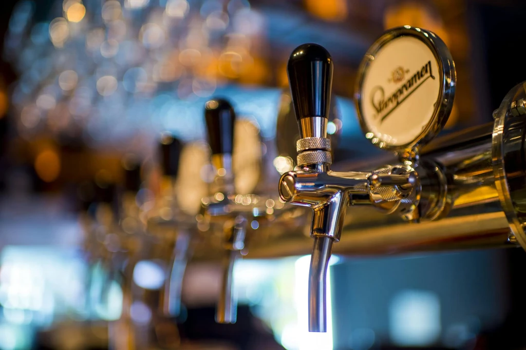 Chrome Staropramen beer tap in focus, other taps blurred in a bar.