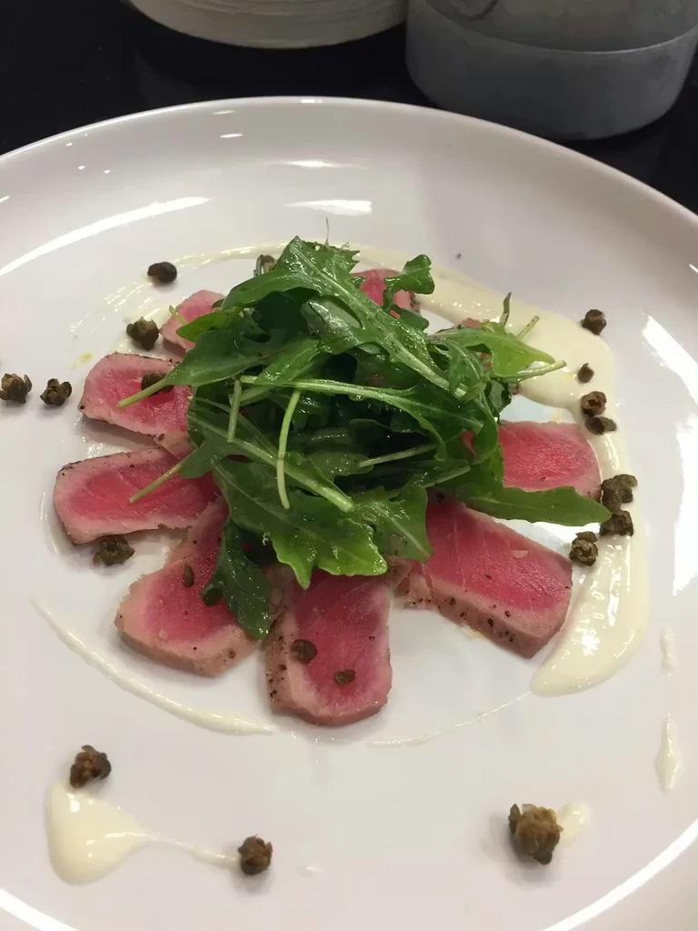 Seared tuna with arugula, capers, and creamy white sauce on a plate.