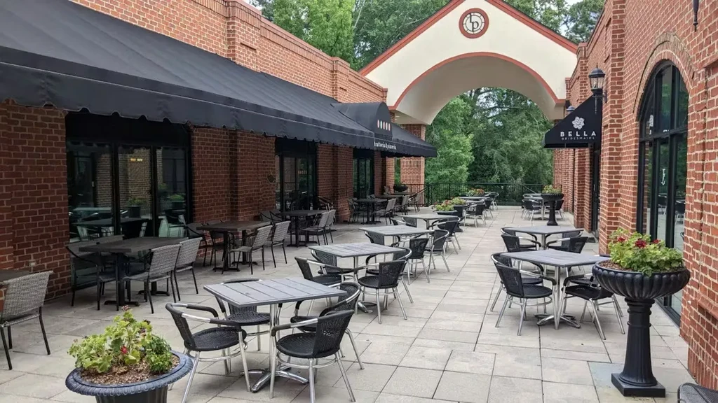 Outdoor trattoria and pizzeria patio with tables and brick archway.