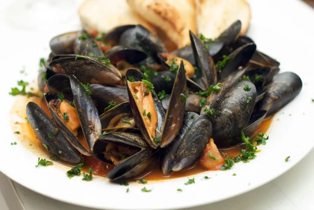 Plate of open steamed mussels in red broth with parsley.