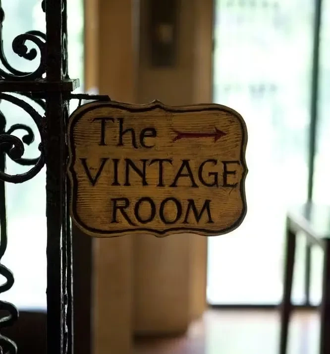 Rustic wooden sign "The VINTAGE ROOM" with arrow, hanging from ornate post.