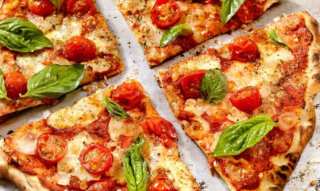 Rustic pizza slices with charred crust, tomatoes, mozzarella, and basil.