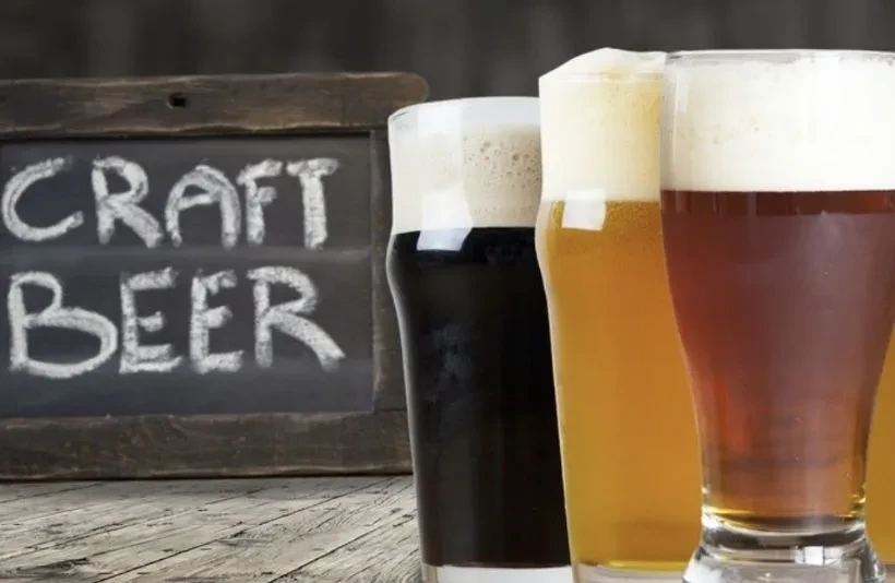 Three craft beers: dark, golden, and reddish, on a wooden table.