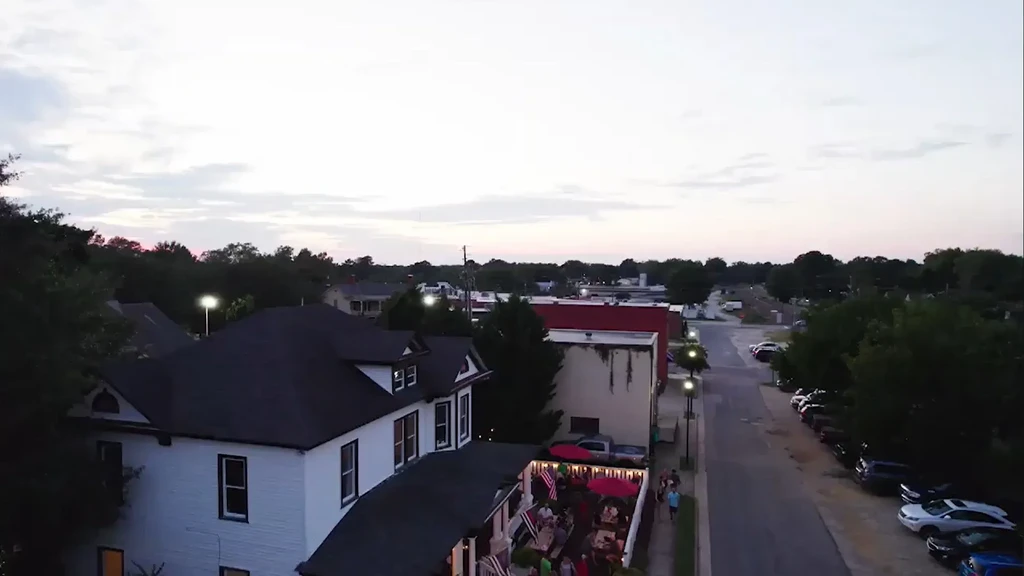 Aerial view: white building with lively patio, red umbrellas at dusk.