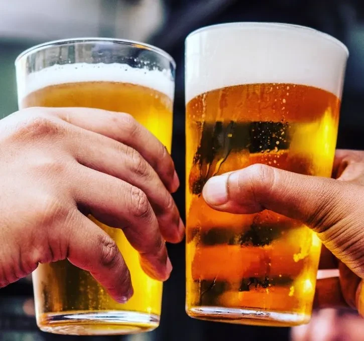 Two hands clinking glasses of golden beer in a toast.