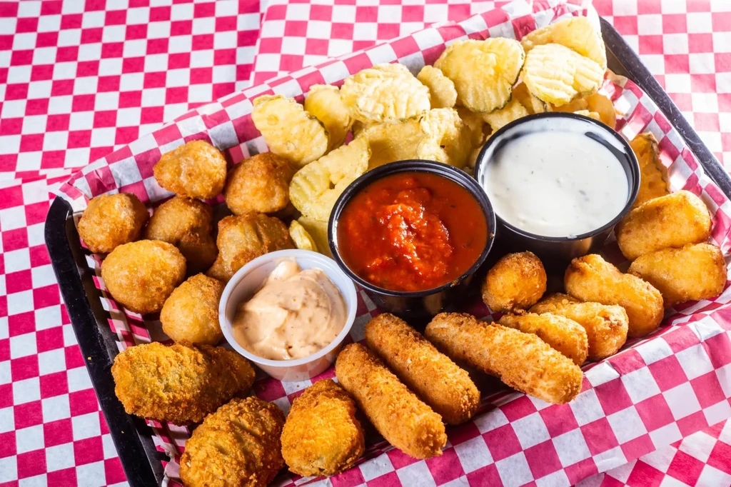 Assorted fried appetizers with three sauces in a checkered lined basket.