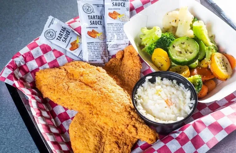 Golden-brown fried fish, coleslaw, steamed vegetables, and tartar sauce.