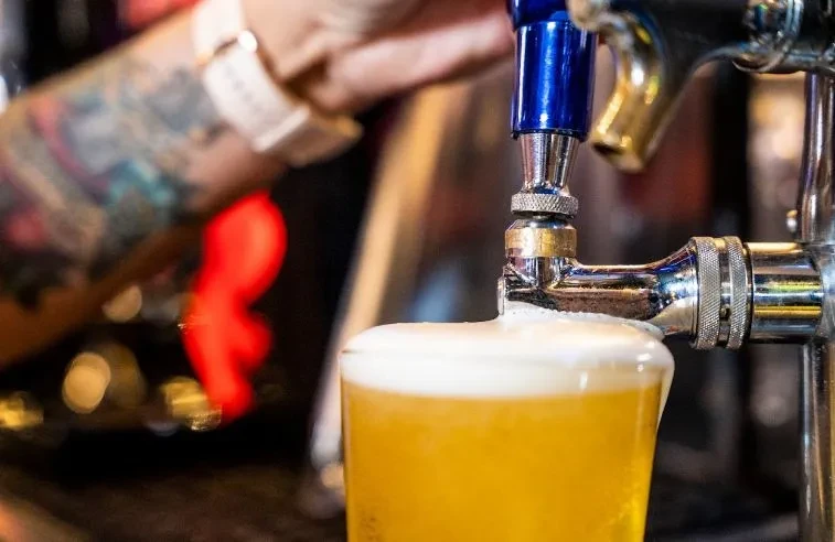 Golden beer overflows from a glass being poured from a tap.
