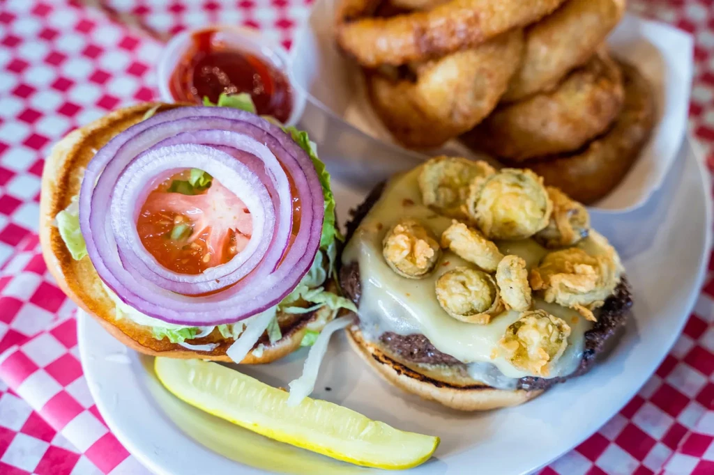 Deconstructed burger with cheese, fried toppings, and onion rings on checkered table.