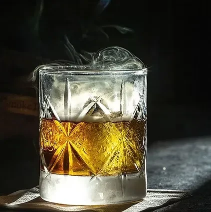 Close-up: Decorated glass with amber liquid and dramatic rising smoke.