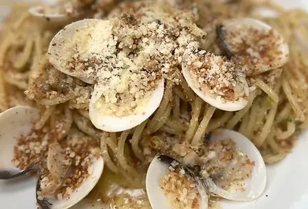 Close-up of spaghetti with breadcrumb-stuffed clams, grated cheese, and pepper.