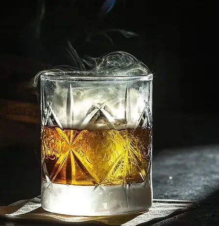 Intricate cut-glass tumbler filled with amber liquid and a plume of smoke.