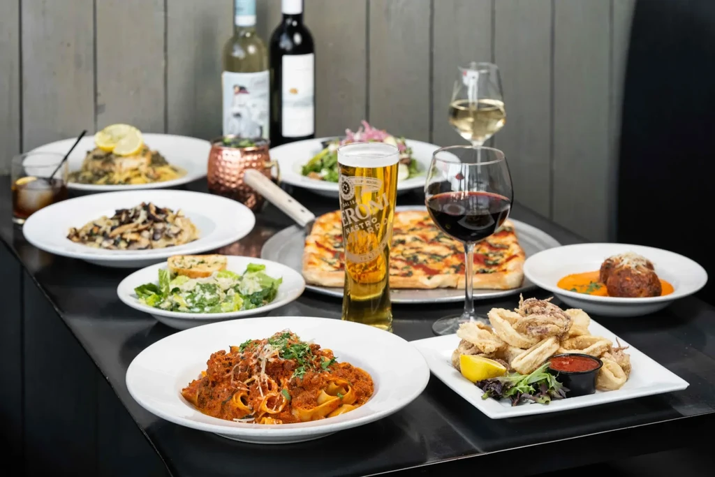 Vibrant spread of Italian pasta, calamari, pizza, drinks on a dark table.