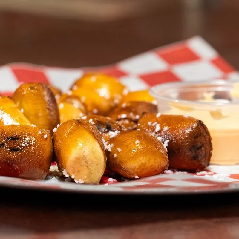 Salted pretzel bites and yellow dipping sauce on a checkered plate.
