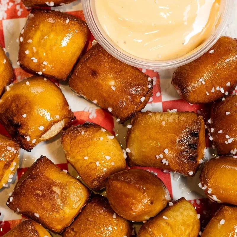 Golden-brown salted pretzel bites, with creamy orange-yellow dipping sauce.