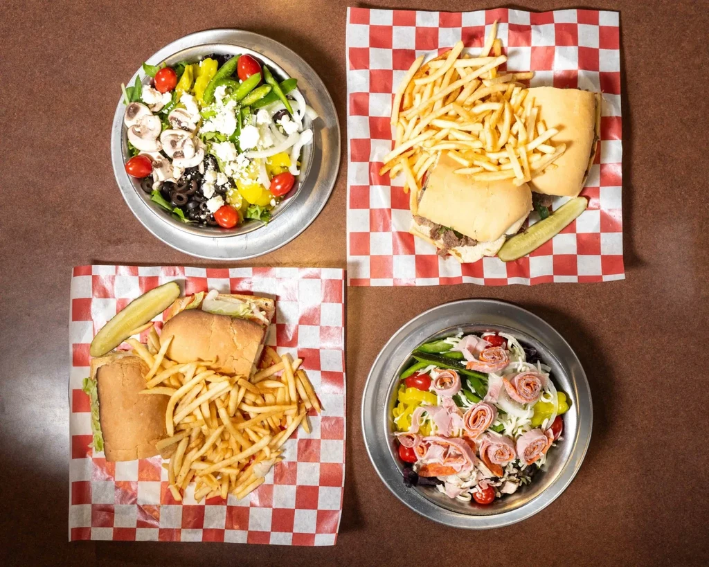 Overhead shot of two salads and two sub sandwiches with fries.