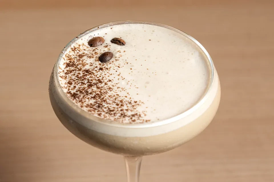 Espresso martini with foam, cocoa powder, and three coffee beans.