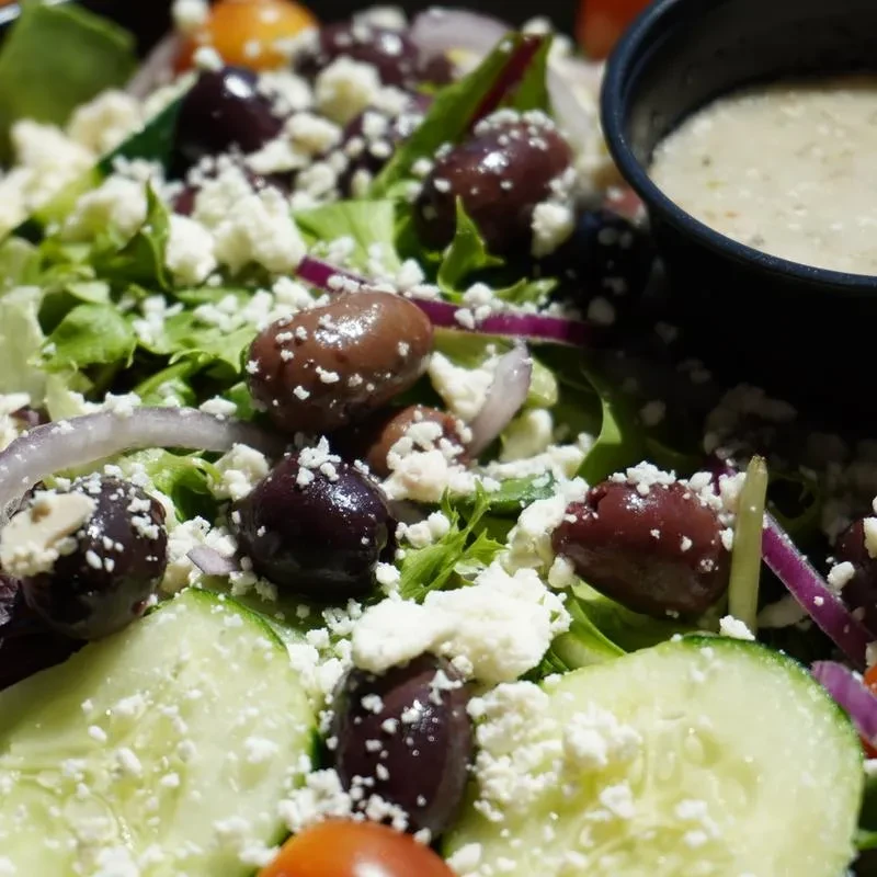 A close-up of a Greek salad with olives, feta, and dressing.