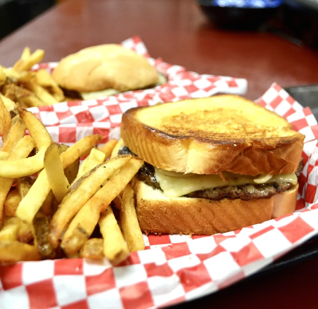 Grilled patty melt with fries in a checkered diner basket.