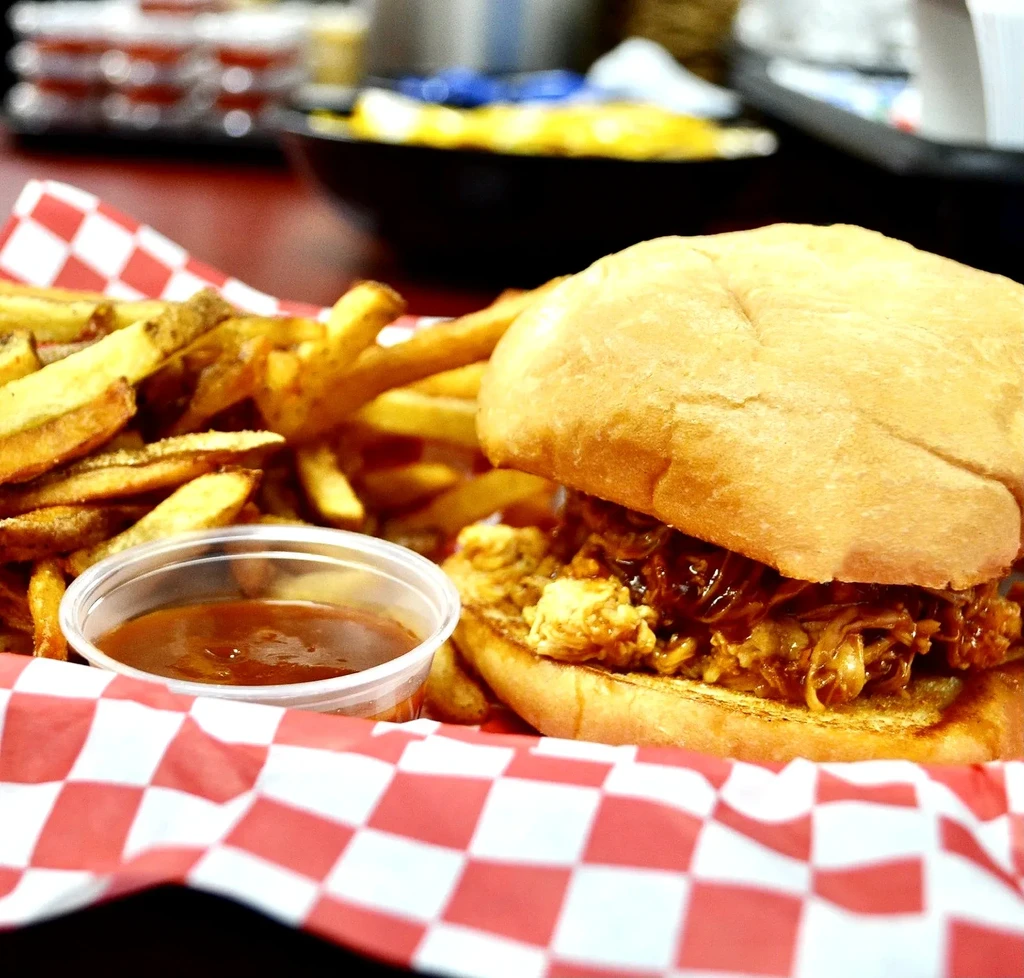 BBQ sandwich, french fries, and dipping sauce on checkered paper.