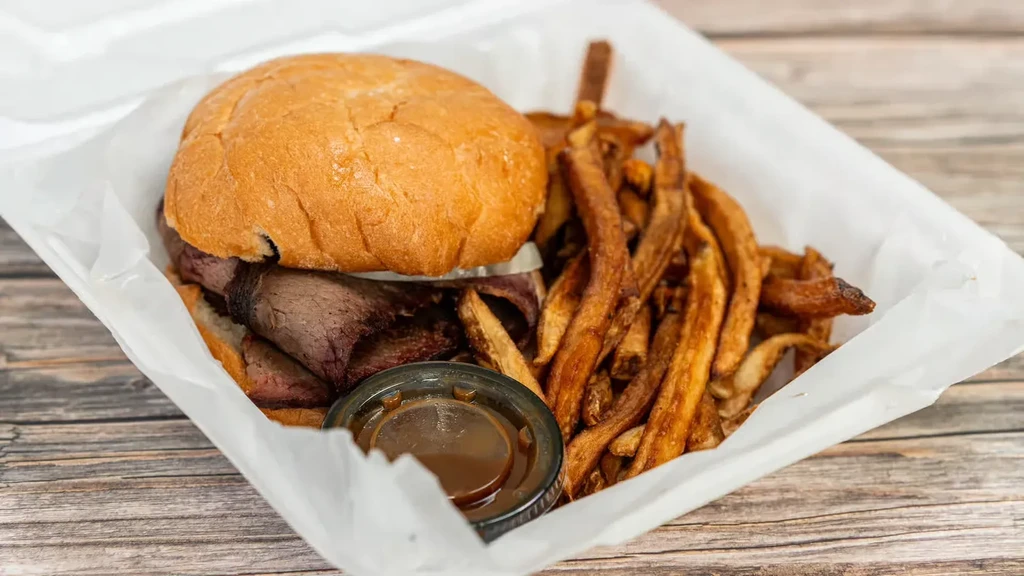 Large sandwich, crispy fries, and dipping sauce in a takeout box.