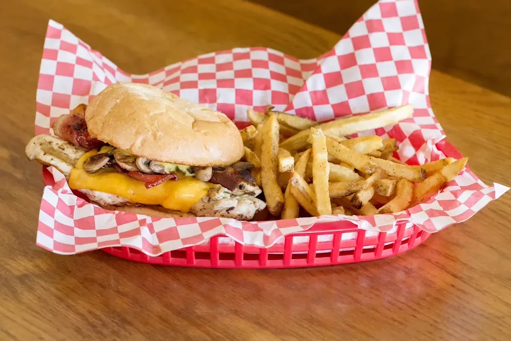Chicken sandwich with cheese, bacon, mushrooms, and fries in a basket.