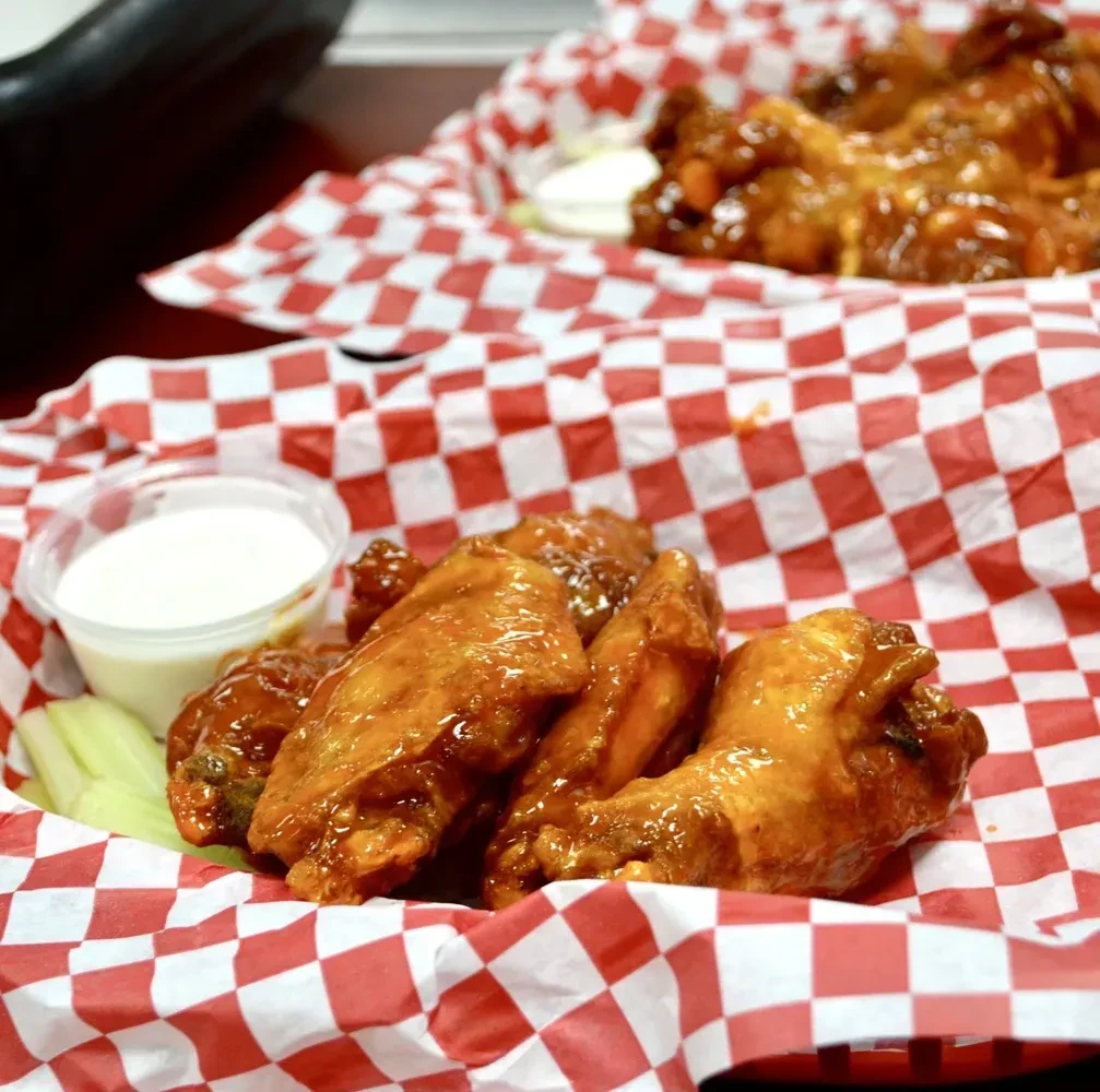Two servings of sauced chicken wings with dip and celery in baskets.
