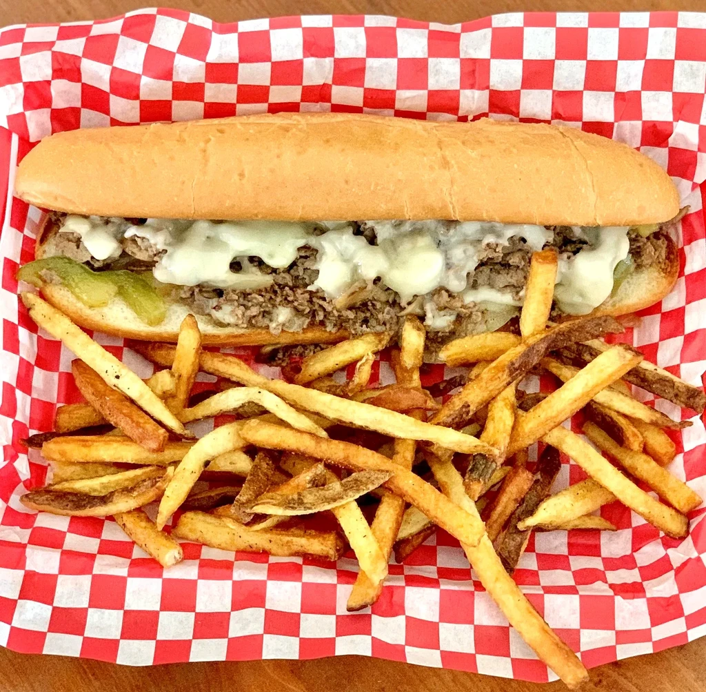 Top-down view of a cheesesteak with melted cheese, peppers, and fries.