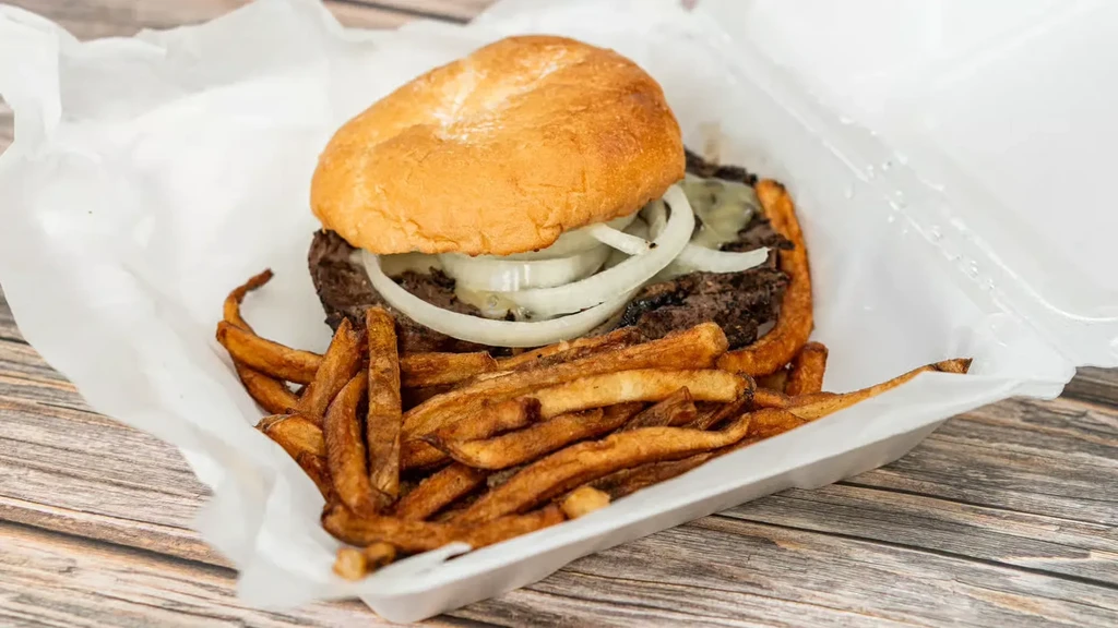 Burger, cheese, onions, and skin-on fries in a styrofoam takeout container.