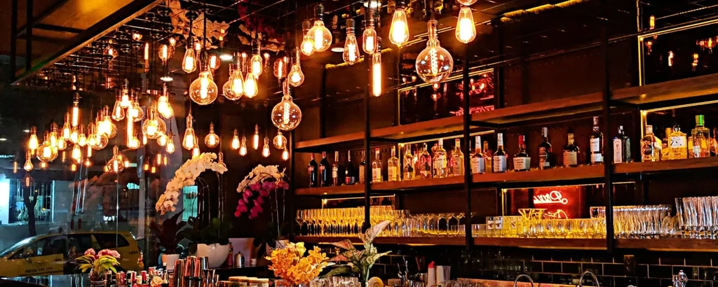 Warm, golden-lit bar interior with Edison bulbs, stocked bar.
