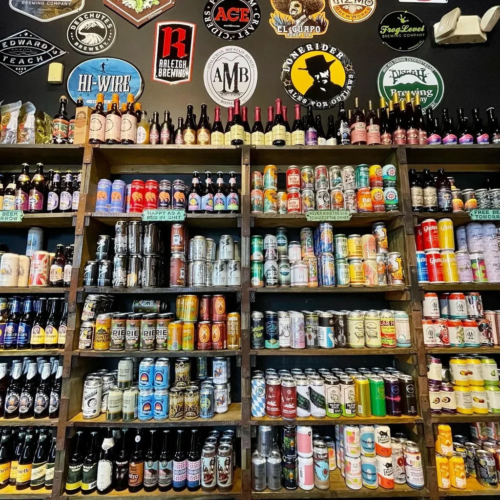 Floor-to-ceiling craft beer collection on rustic shelves with brewery logos.