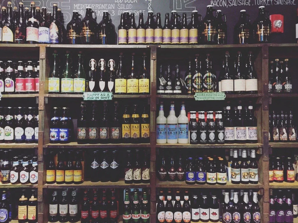 Rustic pub shelves filled floor-to-ceiling with diverse craft beer bottles.