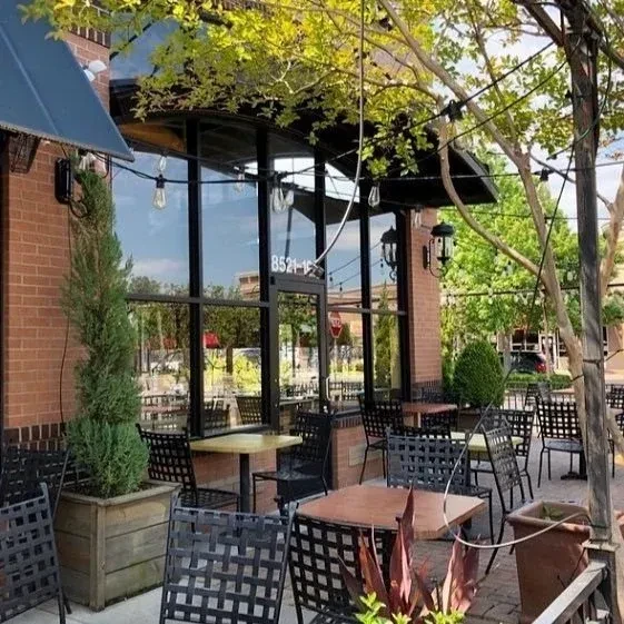 Sunny restaurant patio with metal tables, chairs, brick building, and string lights.