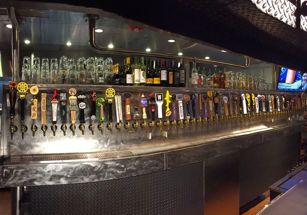 Modern stainless steel bar counter with dozens of beer taps.