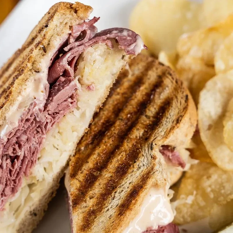 A Reuben sandwich cut in half on a white plate with chips.