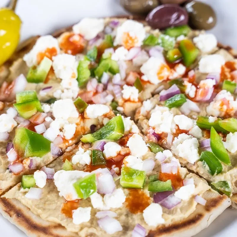 Sliced hummus flatbread with feta, bell peppers, red onions, and drizzle.