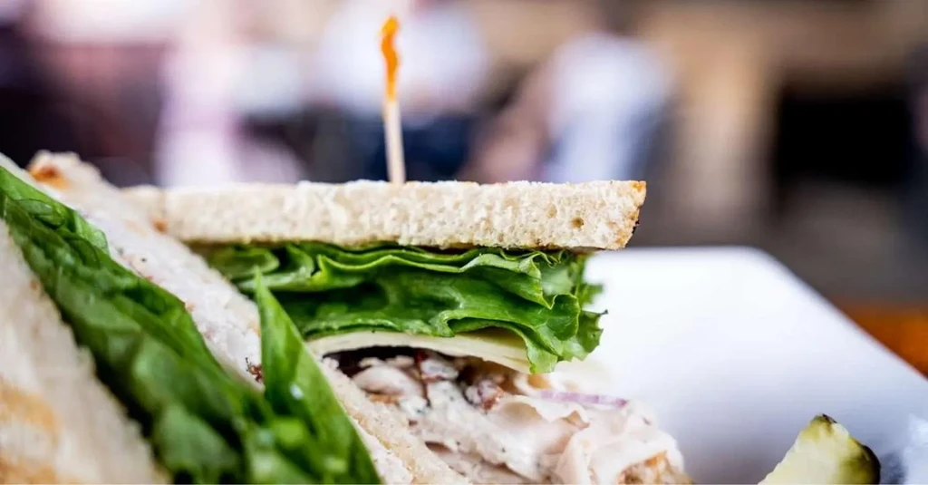 Diagonally cut chicken salad sandwich with lettuce, cheese, and pickle.