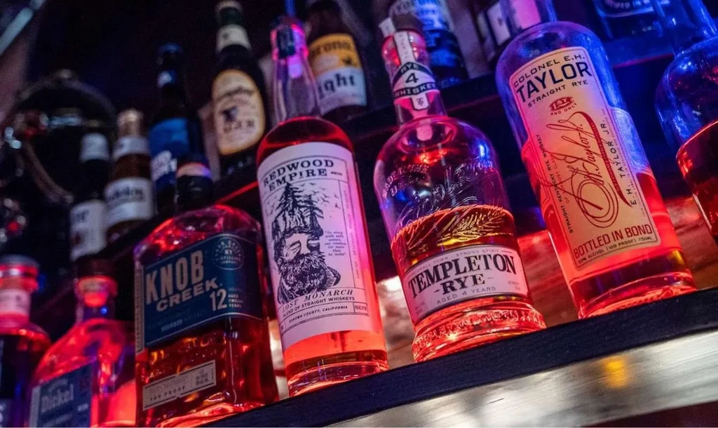 Assorted whiskey and rye bottles dramatically lit on a bar shelf.